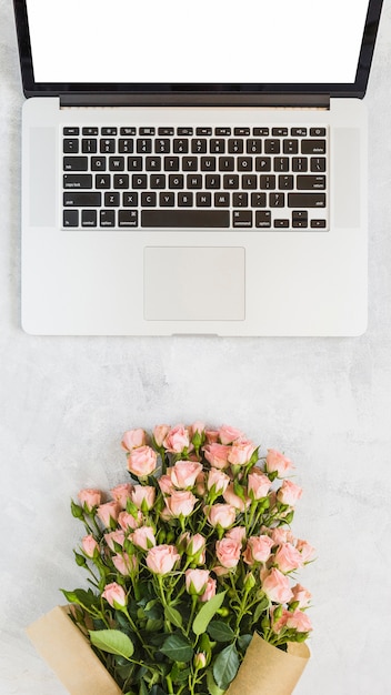 Ramo de rosas frente a una computadora portátil abierta con pantalla en blanco en blanco