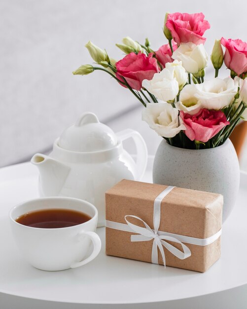 Ramo de rosas en un jarrón junto a un regalo envuelto y una taza de té