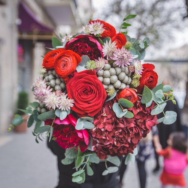 Un ramo de rosas rojas, peonías y flores decorativas verdes con hojas.