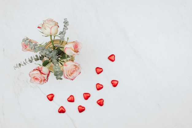 Ramo de rosas de San Valentín con corazones de chocolate rojo sobre un fondo de mármol blanco
