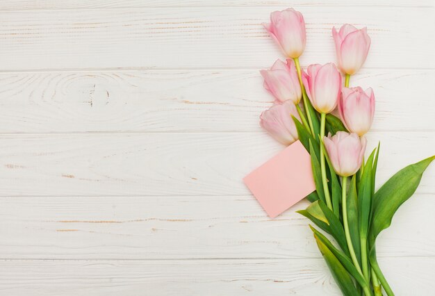 Ramo de tulipán con tarjeta vacía en mesa de madera