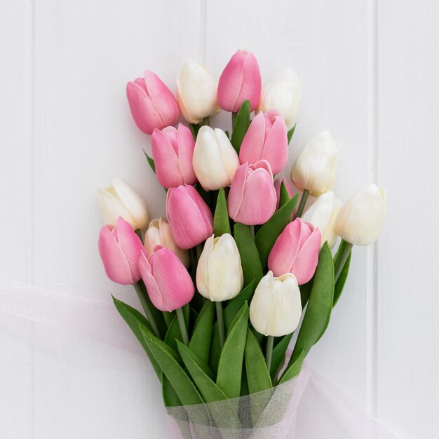 Ramo de tulipanes bastante rosados y blancos sobre fondo de madera