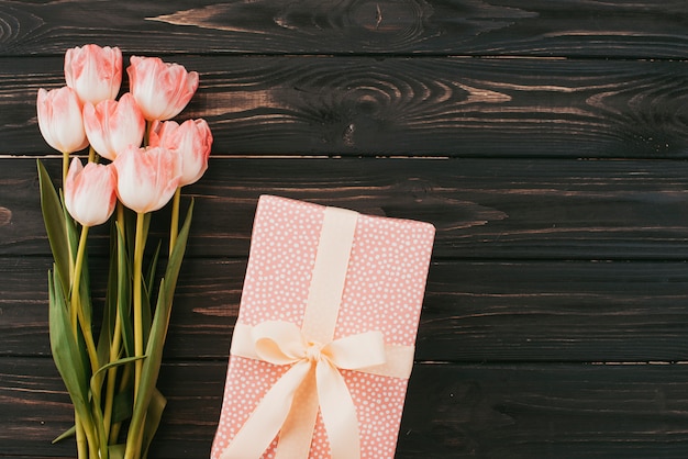 Ramo de tulipanes con caja de regalo en mesa de madera.