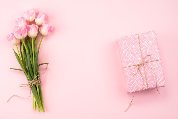 Ramo de tulipanes con caja de regalo en mesa rosa.
