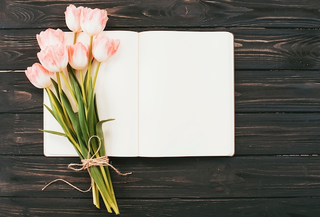 Ramo de tulipanes con cuaderno en blanco en mesa