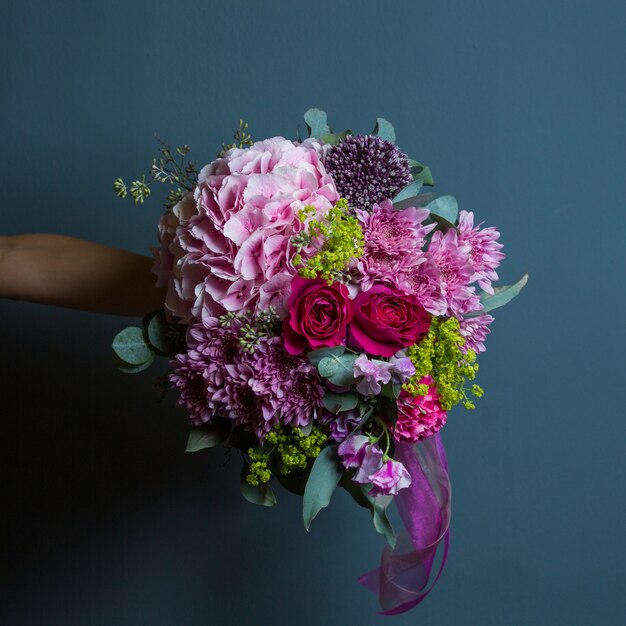 Un ramo de variedad de flores con colores vivos y hojas en las manos de una novia en la pared.