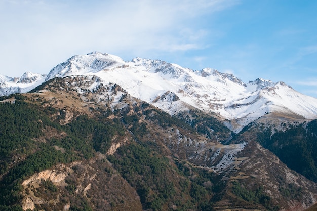 Rango de altas montañas rocosas cubiertas de nieve bajo el cielo nublado