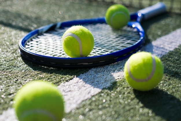 Raqueta de tenis de primer plano y pelotas en el suelo