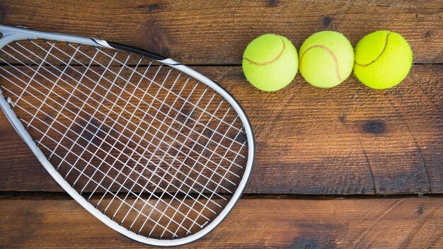 Raqueta de tenis con tres bolas sobre fondo de madera con textura