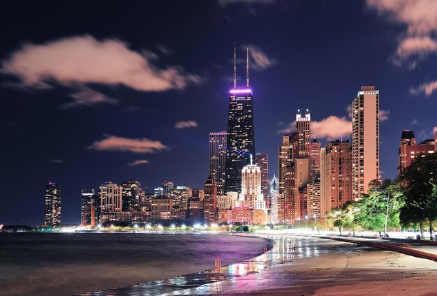 Rascacielos urbanos de la ciudad de Chicago por la noche en el centro de la ciudad frente al lago iluminado con el lago Michigan y el reflejo del agua visto desde North Avenue Beach.