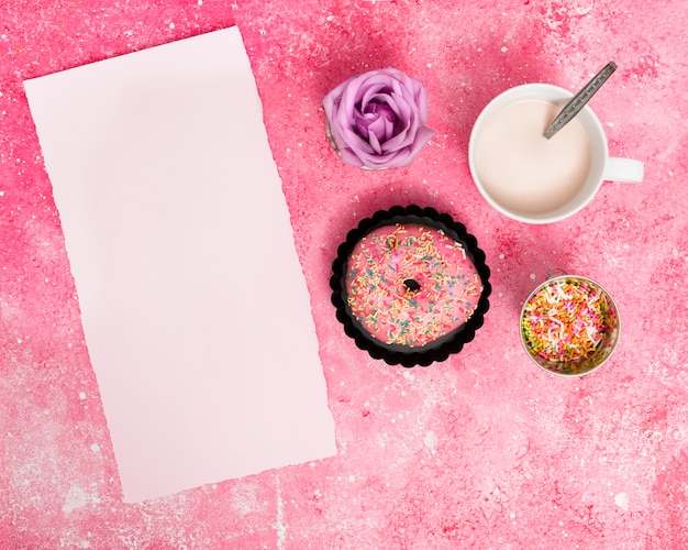 Rasgado de papel blanco en blanco con sprinkles; rosquilla; rosa y leche sobre fondo rosa texturado.