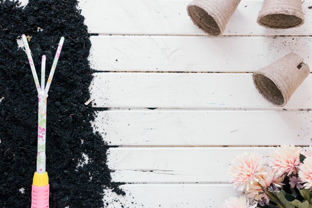 Rastrillo de jardinería en el suelo sobre la mesa de madera con maceta de turba y flores