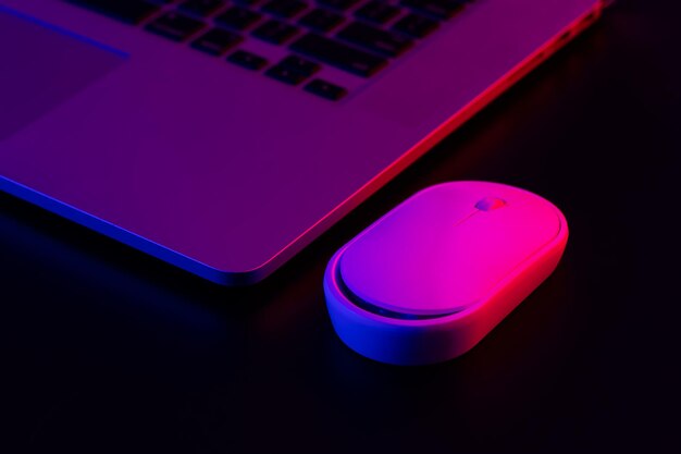 Ratón de la computadora cerca de una computadora portátil en primer plano de iluminación de neón