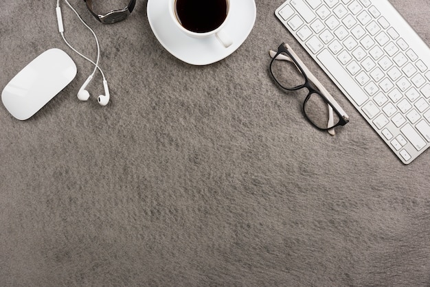 Ratón; teclado; taza de café; teléfono del oído reloj de pulsera sobre fondo gris