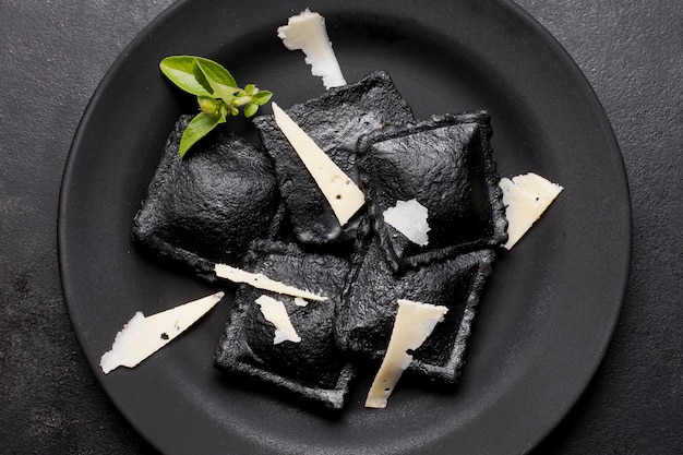 Ravioles negros planos en plato oscuro con lonchas de queso