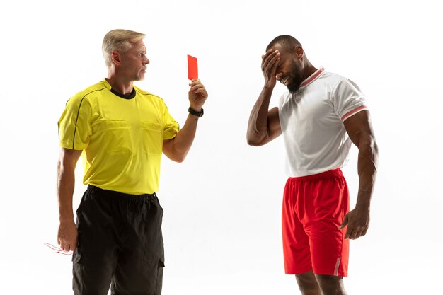 Árbitro que muestra una tarjeta roja a un jugador de fútbol o fútbol afroamericano disgustado mientras juega aislado sobre fondo blanco.