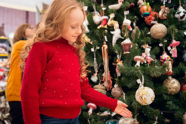 Árbol de Navidad. Familia sonriente, madre e hijos en busca de decoración del hogar y regalos navideños en la tienda del hogar. Cosas retro con estilo para saludos o diseño. Renovación interior, celebrando el tiempo.