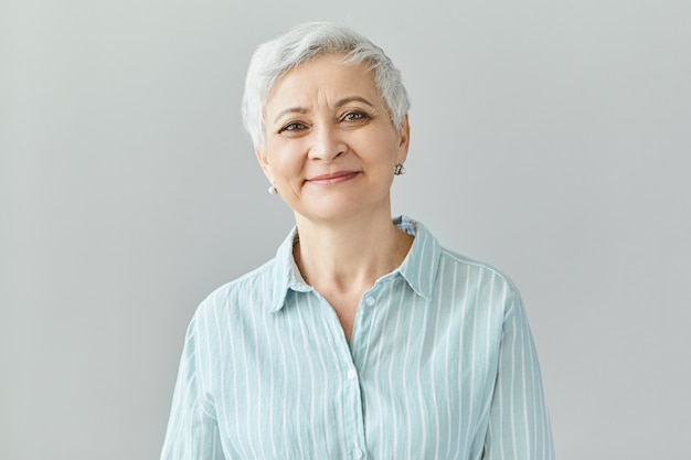 Reacciones, sentimientos y emociones humanas positivas. Encantadora elegante mujer de sesenta años de mediana edad con cabello gris corto con sonrisa de satisfacción, sus ojos llenos de felicidad y alegría