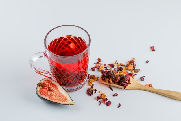 Rebanada de higos con una taza de té, hierbas secas en blanco, vista de ángulo alto.