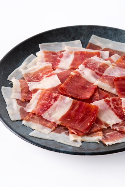 Rebanada de jamón serrano español sobre placa negra aislado sobre fondo blanco.