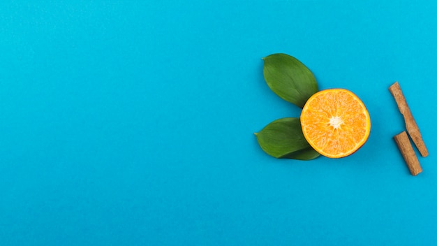 Rebanada de naranja fresca cerca de canela y follaje