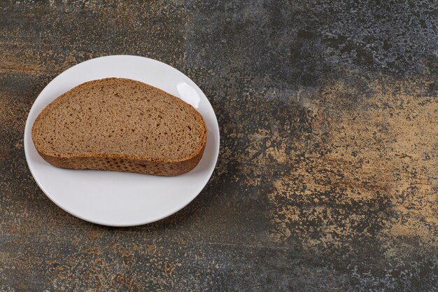 Una rebanada de pan negro en la placa blanca.