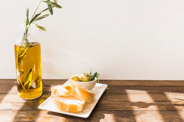 Rebanada de pan con tazón de aceitunas en la mesa de madera