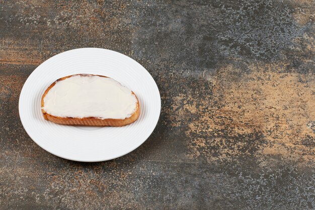 Rebanada de pan tostado con crema agria en un plato blanco.