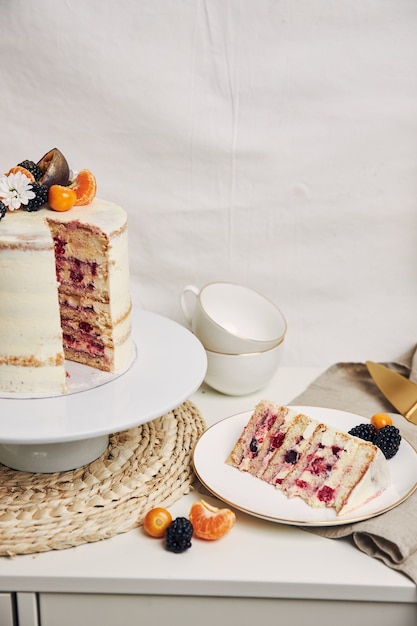 Rebanada de pastel con bayas y maracuyá en la mesa detrás de un fondo blanco.