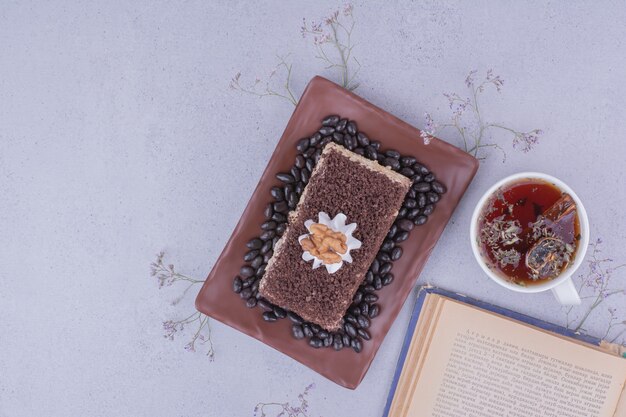 Rebanada de pastel de cacao con nuez y una taza de té de hierbas.