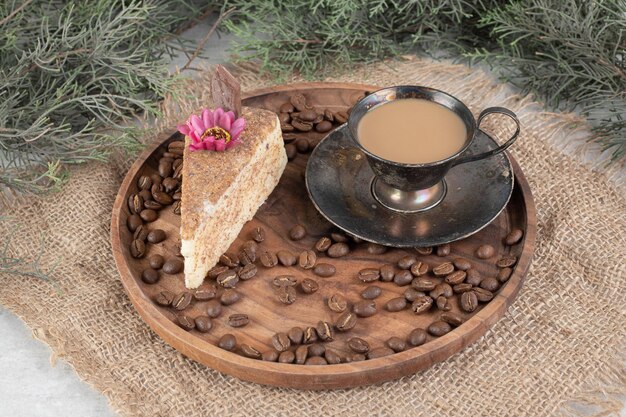Rebanada de pastel, café y granos de café en placa de madera