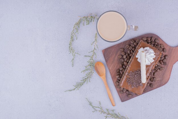 Foto gratuita una rebanada de pastel de caramelo en una bandeja de madera con un vaso de café con leche