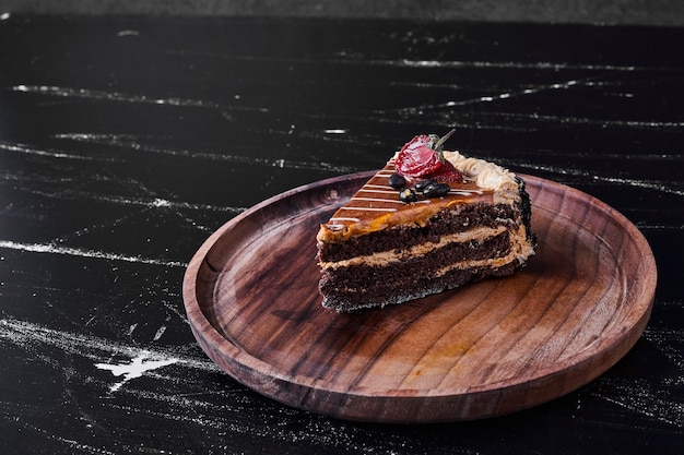 Una rebanada de pastel de caramelo de chocolate en una placa de madera.