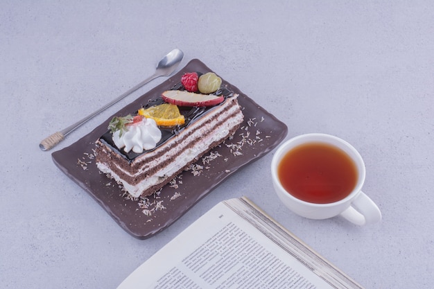 Una rebanada de pastel de chocolate con frutas y una taza de bebida.