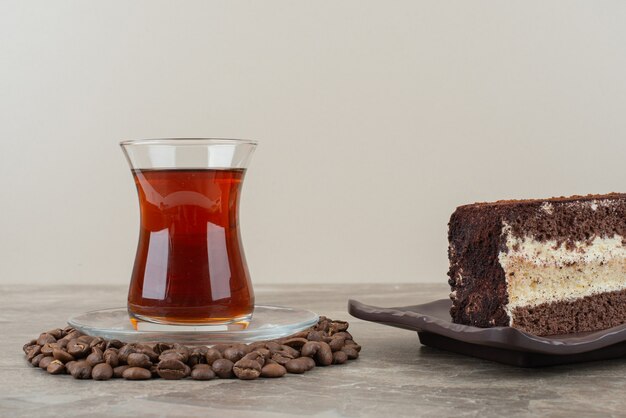 Rebanada de pastel de chocolate, granos de café y vaso de té en la mesa de mármol.