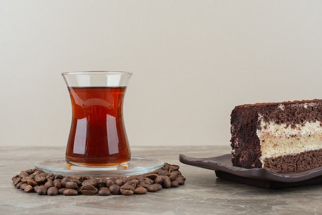 Rebanada de pastel de chocolate, granos de café y vaso de té en la mesa de mármol.