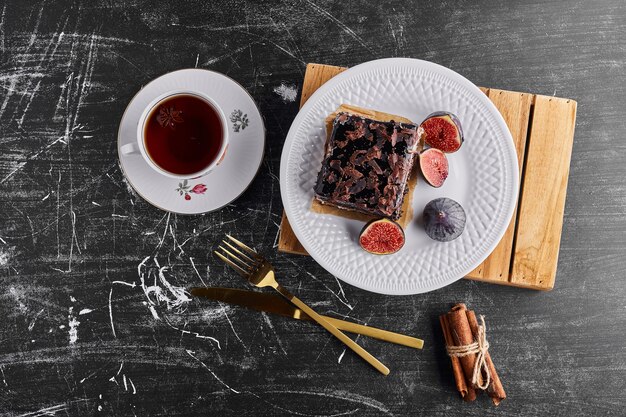 Una rebanada de pastel de chocolate con higos y té en un plato blanco.