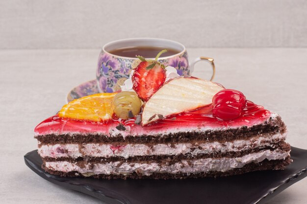 Rebanada de pastel de chocolate en un plato con rodajas de frutas y una taza de té.