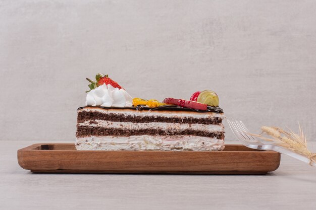 Rebanada de pastel de chocolate sobre tabla de madera con rodajas de frutas.