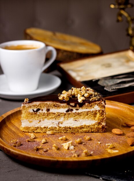 Rebanada de pastel con cobertura de chocolate y nueces servidas con una taza de café.
