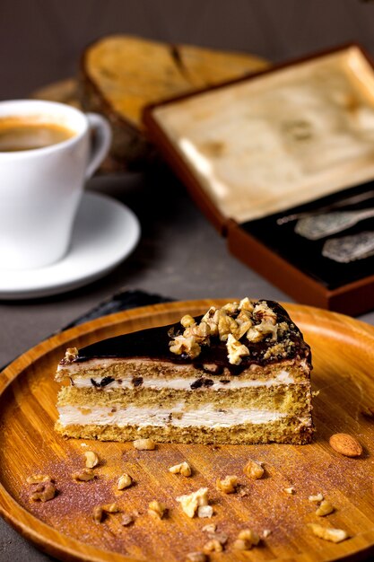 Rebanada de pastel con cobertura de chocolate y nueces servidas con una taza de café.