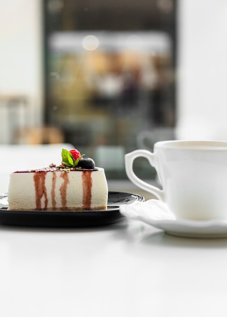 Rebanada de pastel delicioso cerca de la taza de café con leche en la mesa