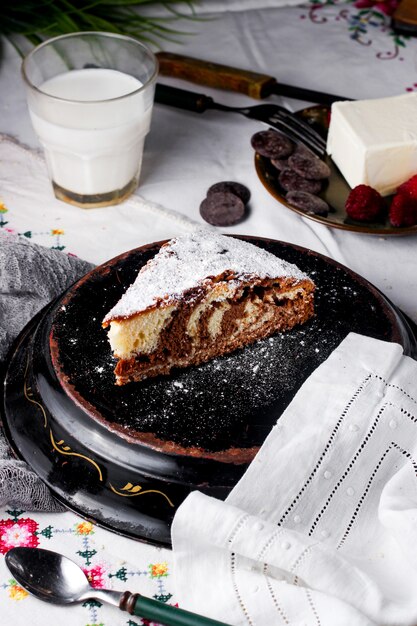 Una rebanada de pastel diurno y nocturno espolvoreado con azúcar en polvo servido con leche