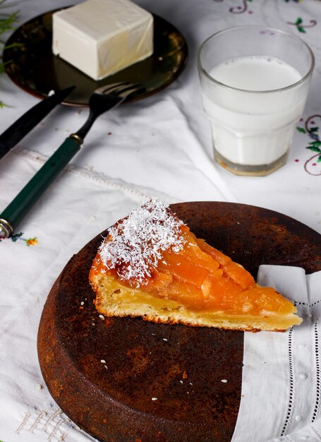 Una rebanada de pastel de durazno espolvoreado con coco rallado servido con mantequilla y leche