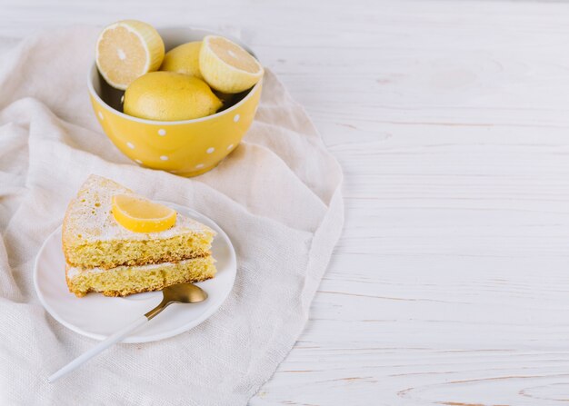 Rebanada de pastel de limón en un plato blanco con limones en rodajas en un tazón