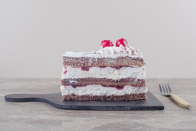 Rebanada de pastel pequeño con cobertura de crema, cereza y cacao en polvo sobre una tabla de mármol