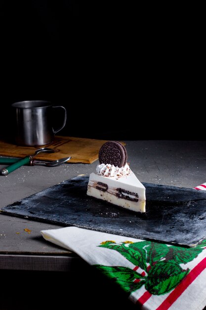 Una rebanada de pastel de queso oreo decorado con galletas oreo y crema blanca