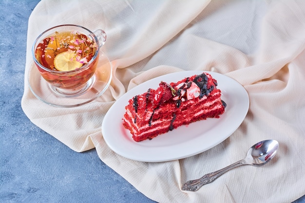 Una rebanada de pastel de terciopelo rojo en un plato blanco con té de hierbas