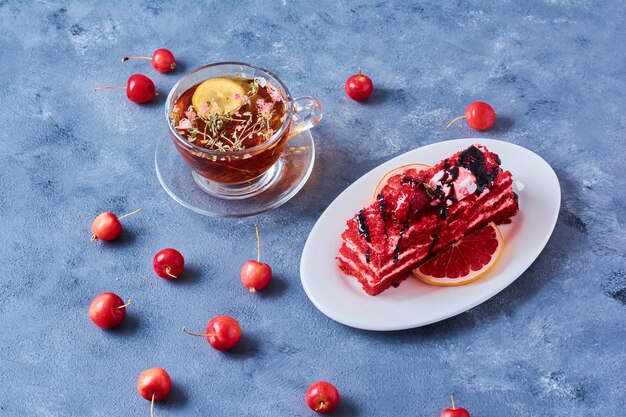 Una rebanada de pastel de terciopelo rojo en un plato blanco con té.