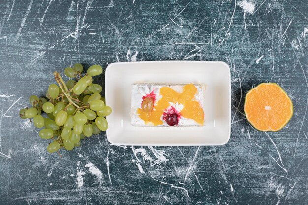 Rebanada de pastel, uvas y naranja sobre fondo azul. Foto de alta calidad